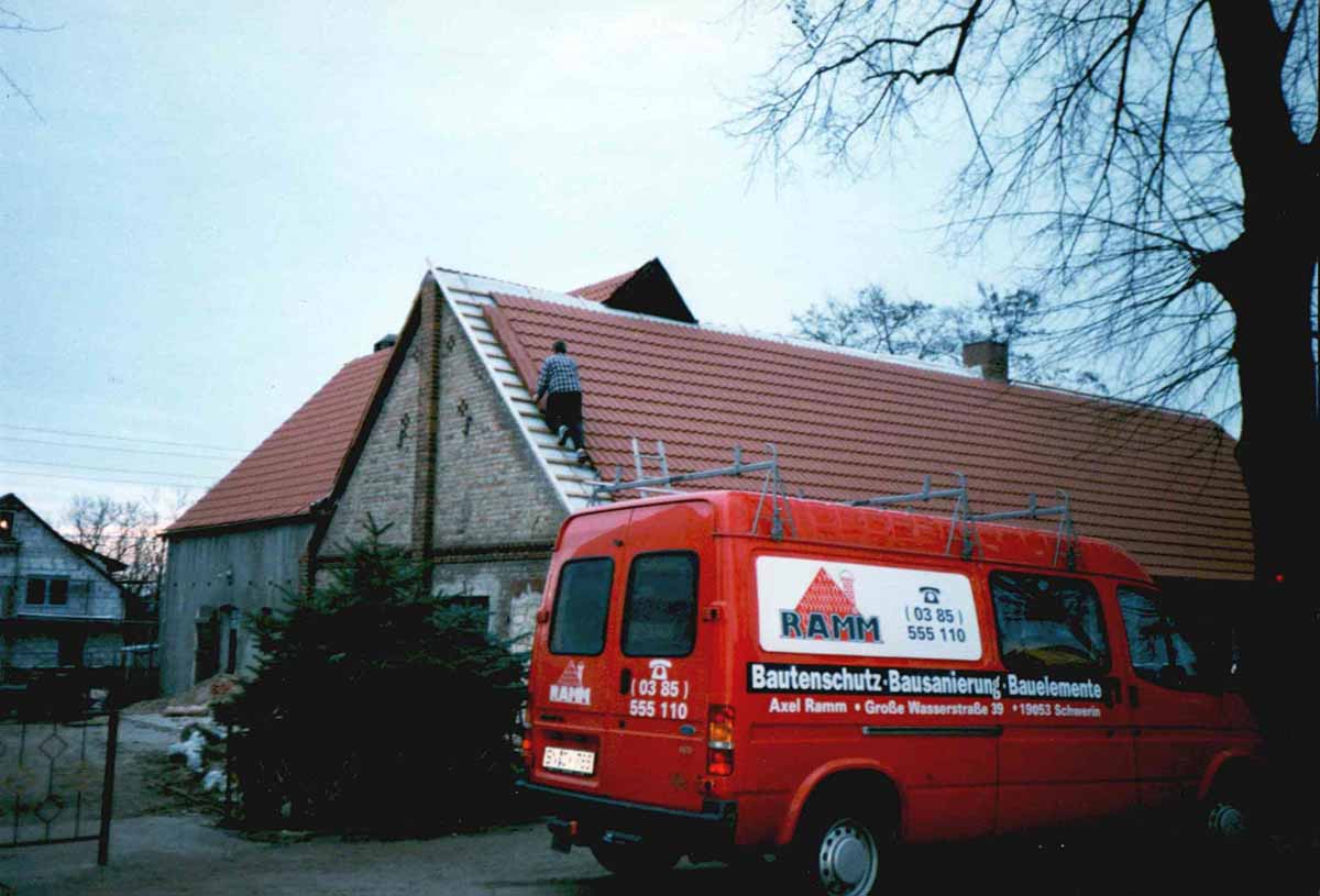 Altes Foto aus den Anfangsjahren: roter Firmenwagen vor einem Klinkerhaus, auf dem Dach wird gearbeitet.