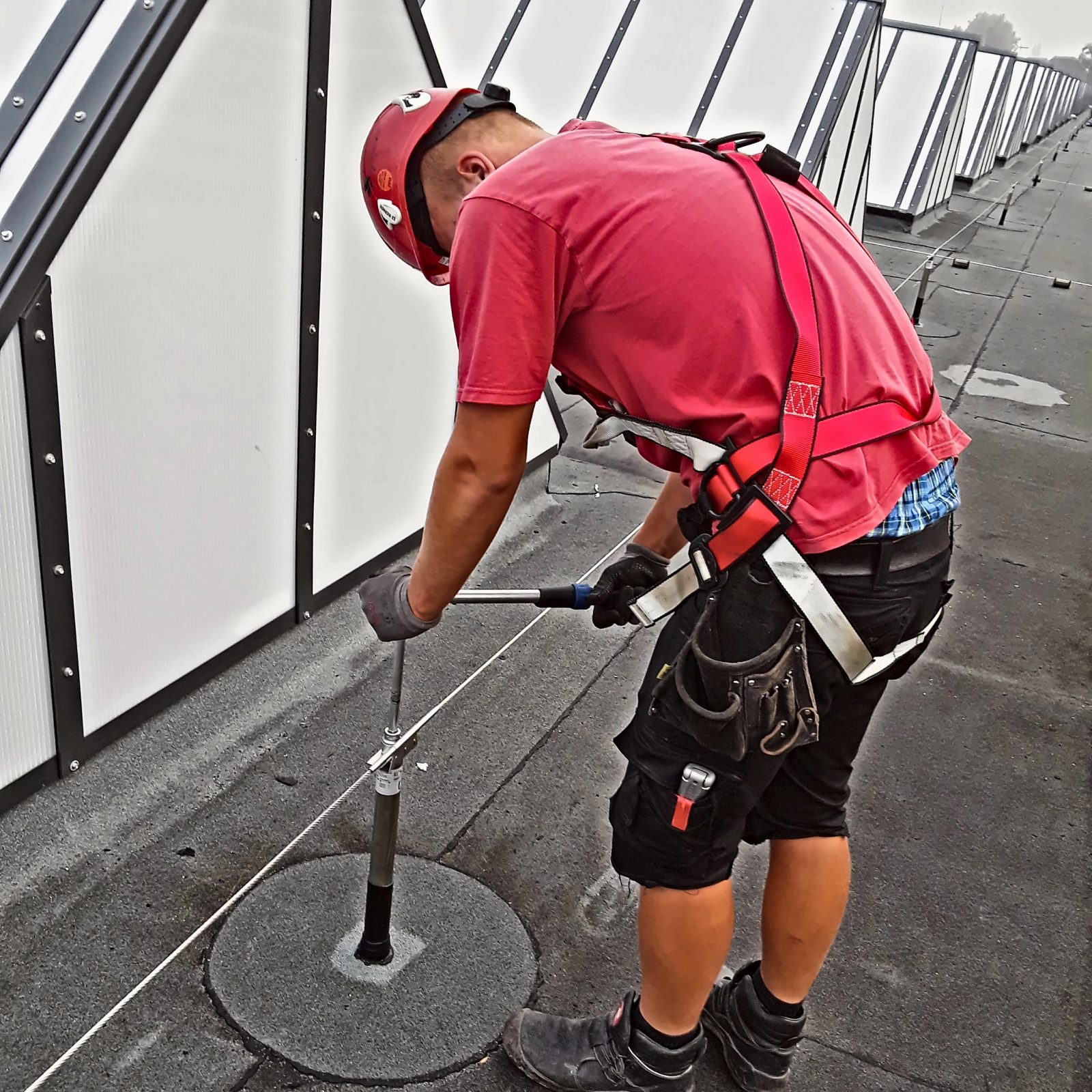 Dachdecker prüft einen Anschlagpunkt auf einem Flachdach mit dem Prüfgerät, Hamburg