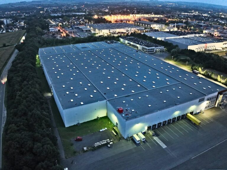 Drohnenaufnahme einer großen Logistikhalle mit Flachdach in der Abenddämmerung, Werl